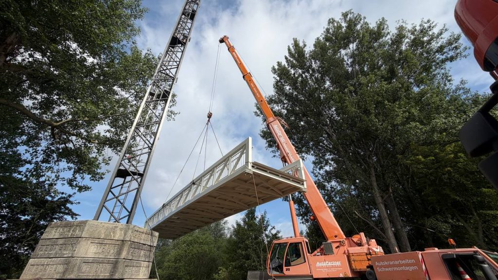 Mobile crane lifting an aluminium bridge span into position over a river