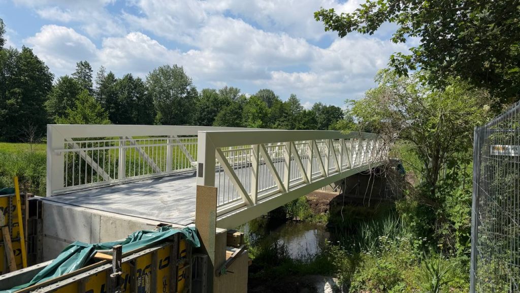 Cream aluminium truss footbridge over a stream with concrete abutment formwork in place