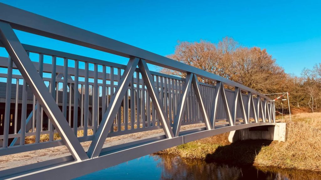 Close view of the truss and railing of a grey aluminium footbridge over water in autumn