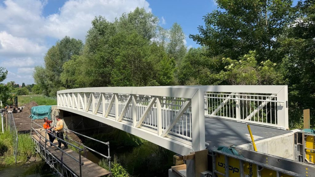 Cream aluminium arched footbridge over a stream with workers finishing the abutment