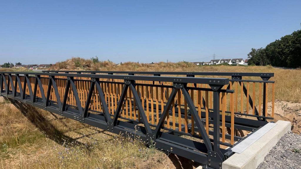 Anthracite aluminium bridge with timber railing infill over a drainage ditch in summer