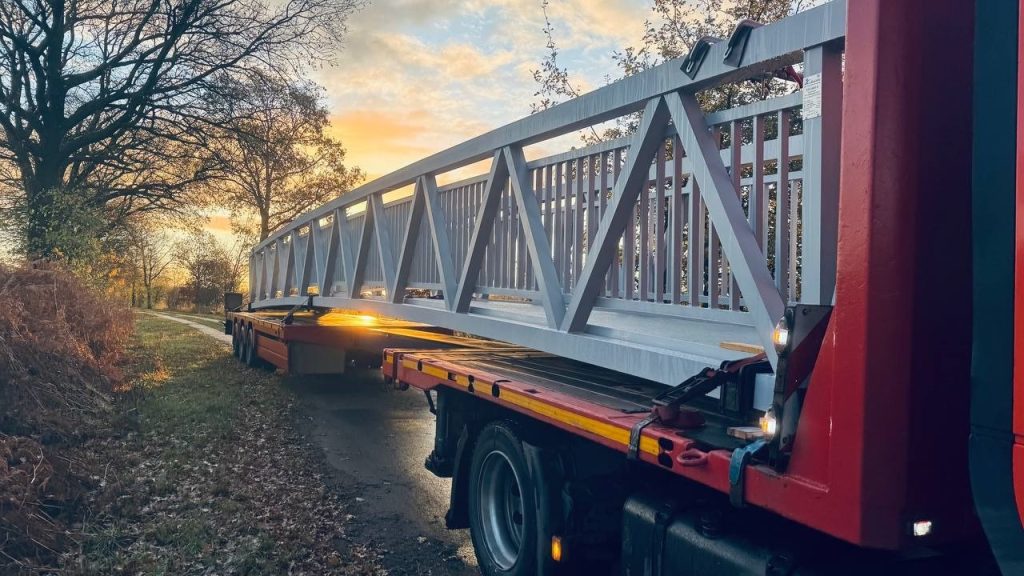 Vaaleanharmaa alumiiniristikkoinen silta matalalavaisella perävaunulla auringonnousun aikaan